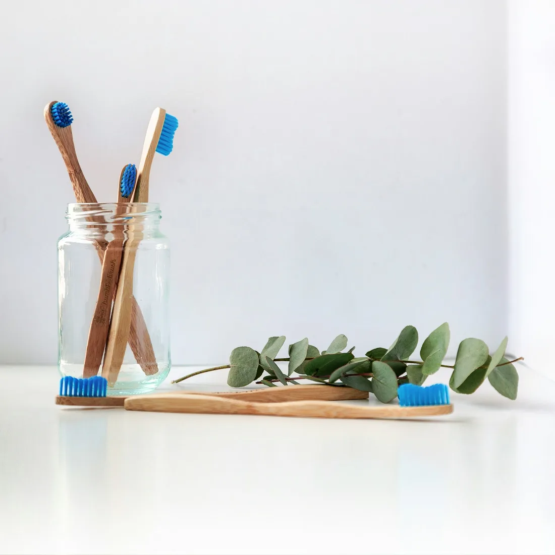 Bamboo toothbrushes in a glass jar on a white surface